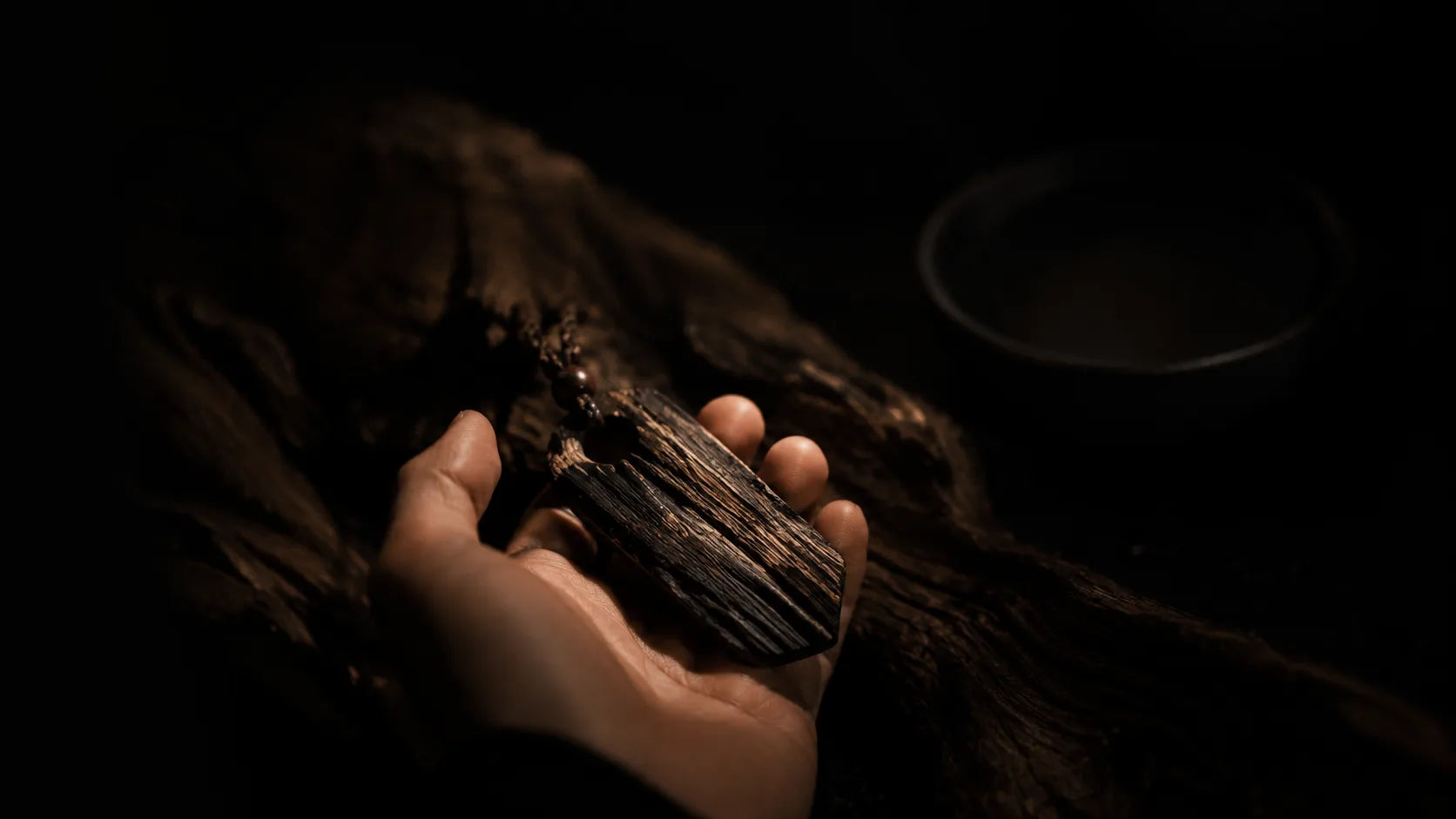 A wooden pendant held in a dark, warm-lit setting
